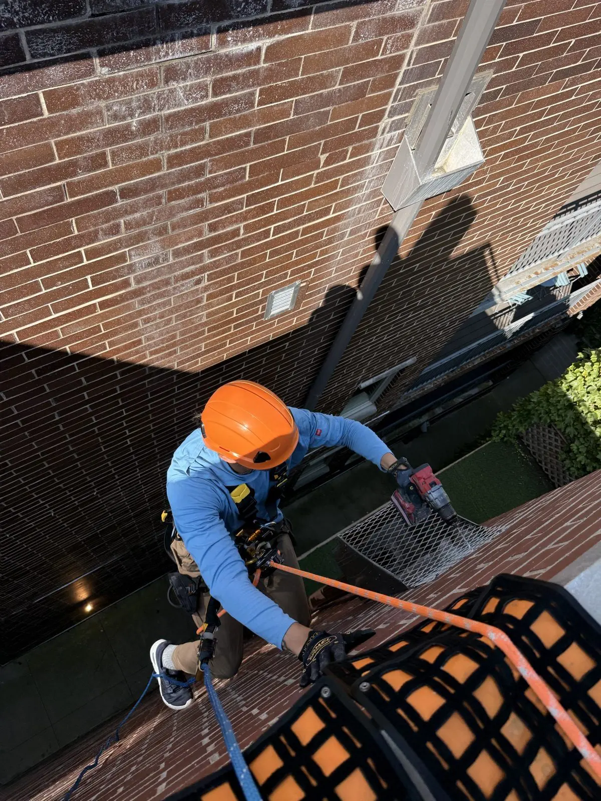 Technician rappelling down a red brick facade toward a fourth-floor downspout in Old Town, Chicago.