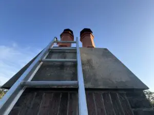 extension ladder against a two-flue chimney with clay toppers