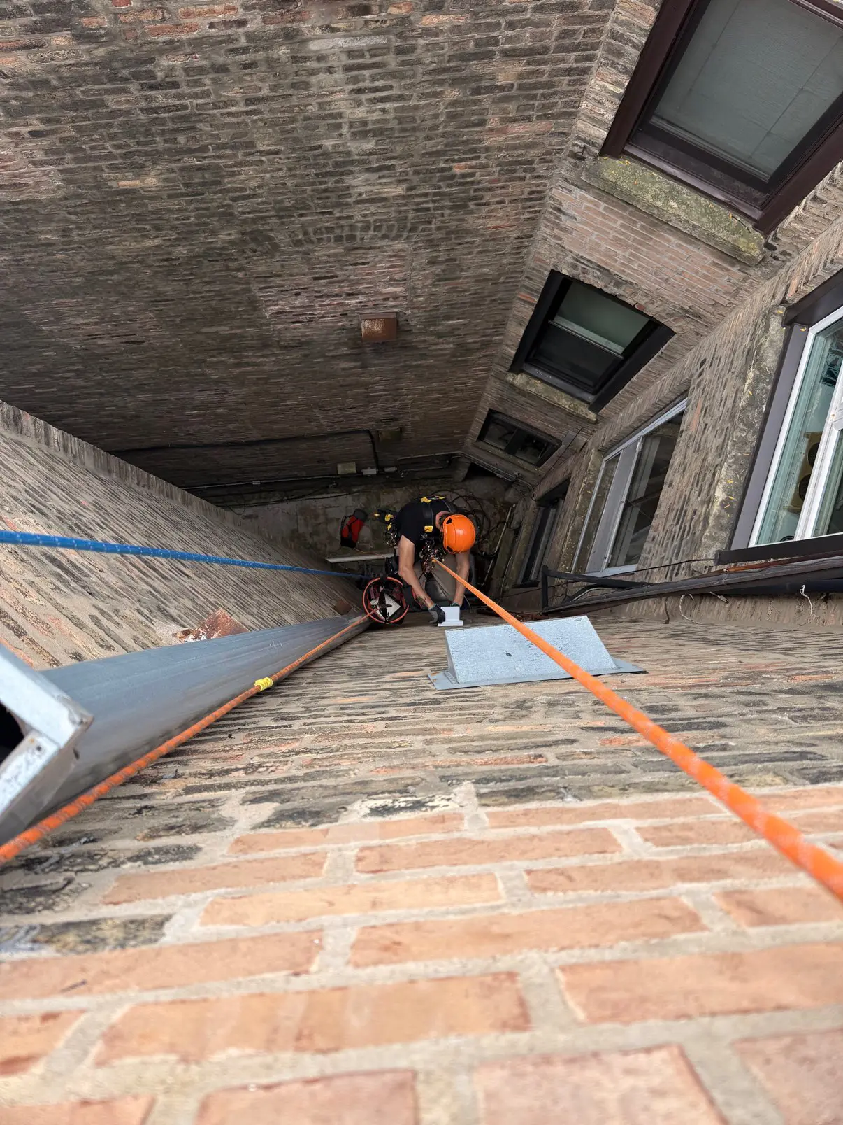Rope-access technician descending between Chicago masonry buildings to reach a high dryer vent