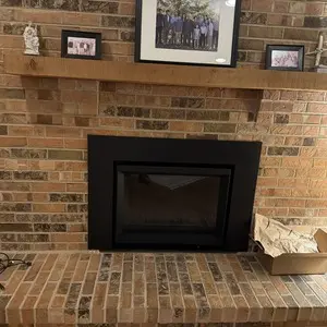 Finished black STUV 6 wood-burning insert installed inside an existing brick fireplace with a raised brick hearth
