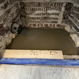 Mason restoring non-combustible support around a fireplace hearth after wood form removal
