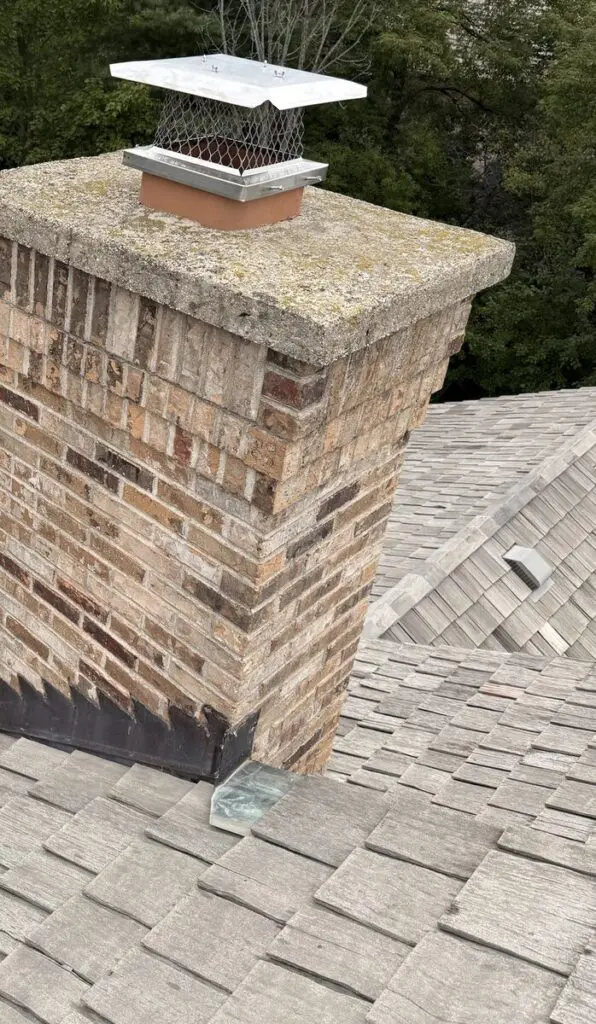 Brick chimney with a stainless steel rain cap with mesh screen on the flue tile