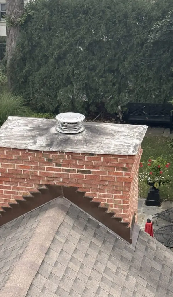 Red brick chimney with metal step flashing along the roofline, a sheet metal top and a stainless steel cap