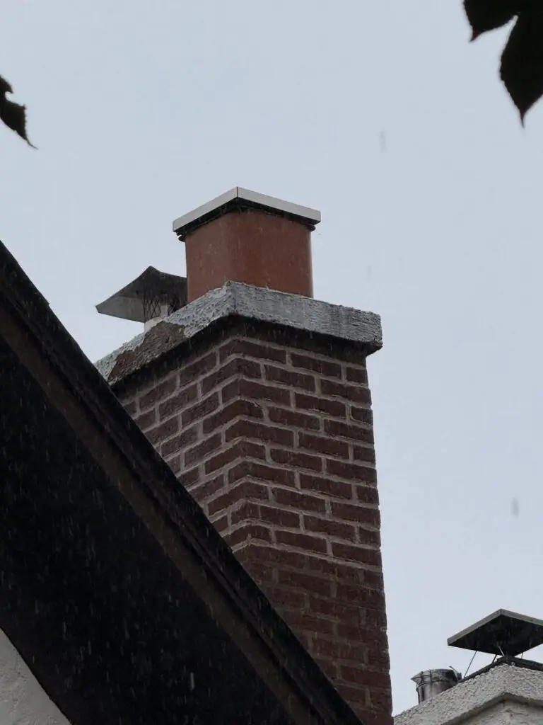 Brick chimney with a worn, uneven mortar crown, a clay flue tile and a stainless steel cap