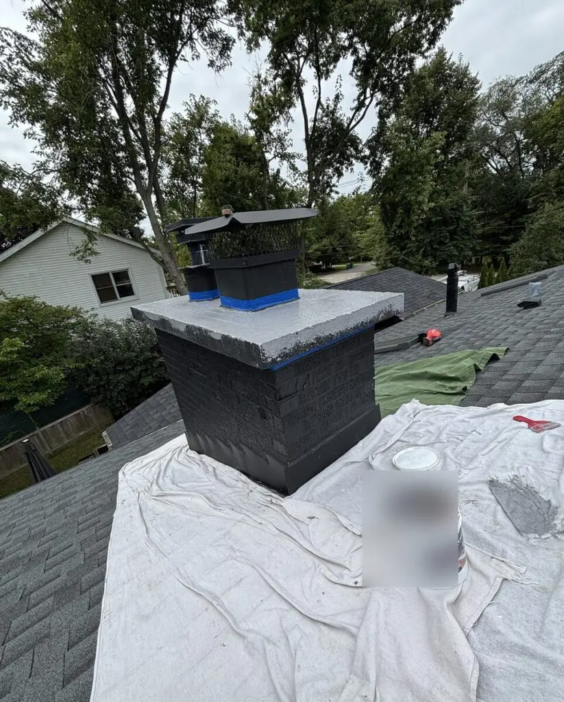Chimney crown during recoating, with drop cloths protecting the roof and blue tape around the flue caps