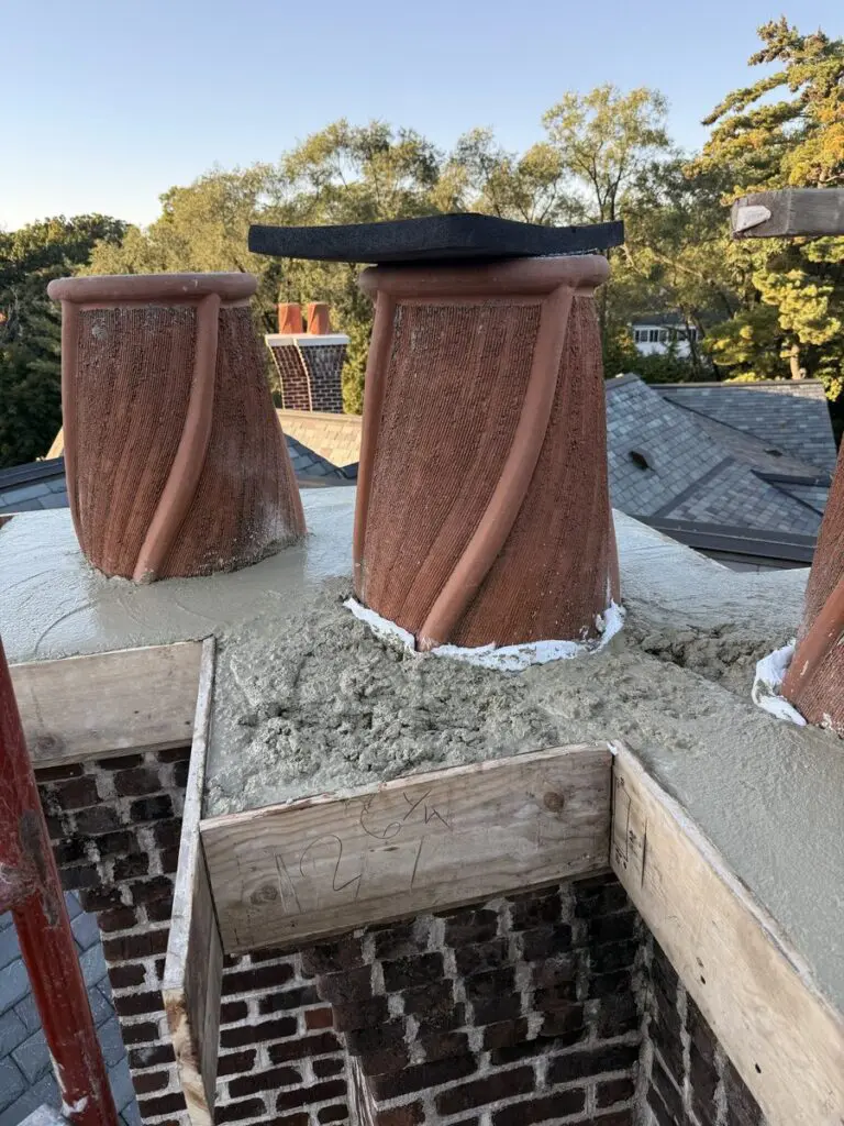 Two twisted clay chimney pots set in a freshly poured concrete crown, with wood forms still in place on the brick chimney