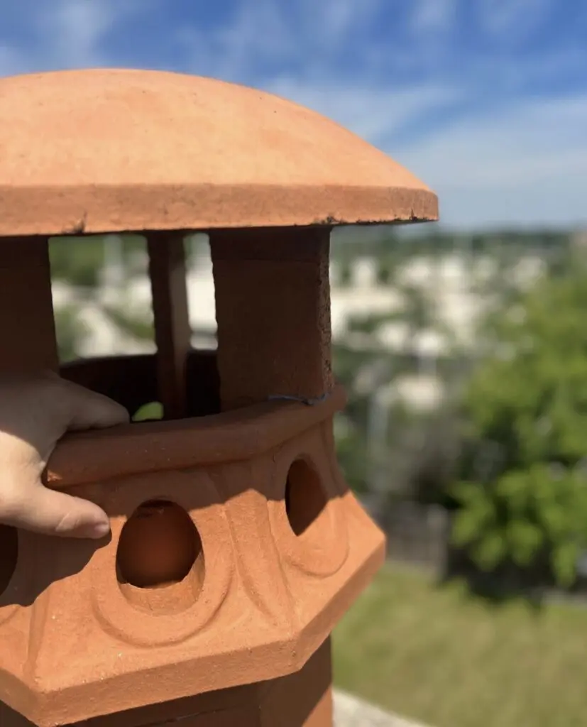 Close-up of a terracotta chimney terminal with a domed top and openings between its supports.