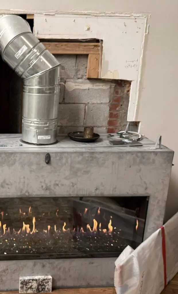 Linear gas fireplace being installed, with the direct vent pipe connected and the burner lit for testing
