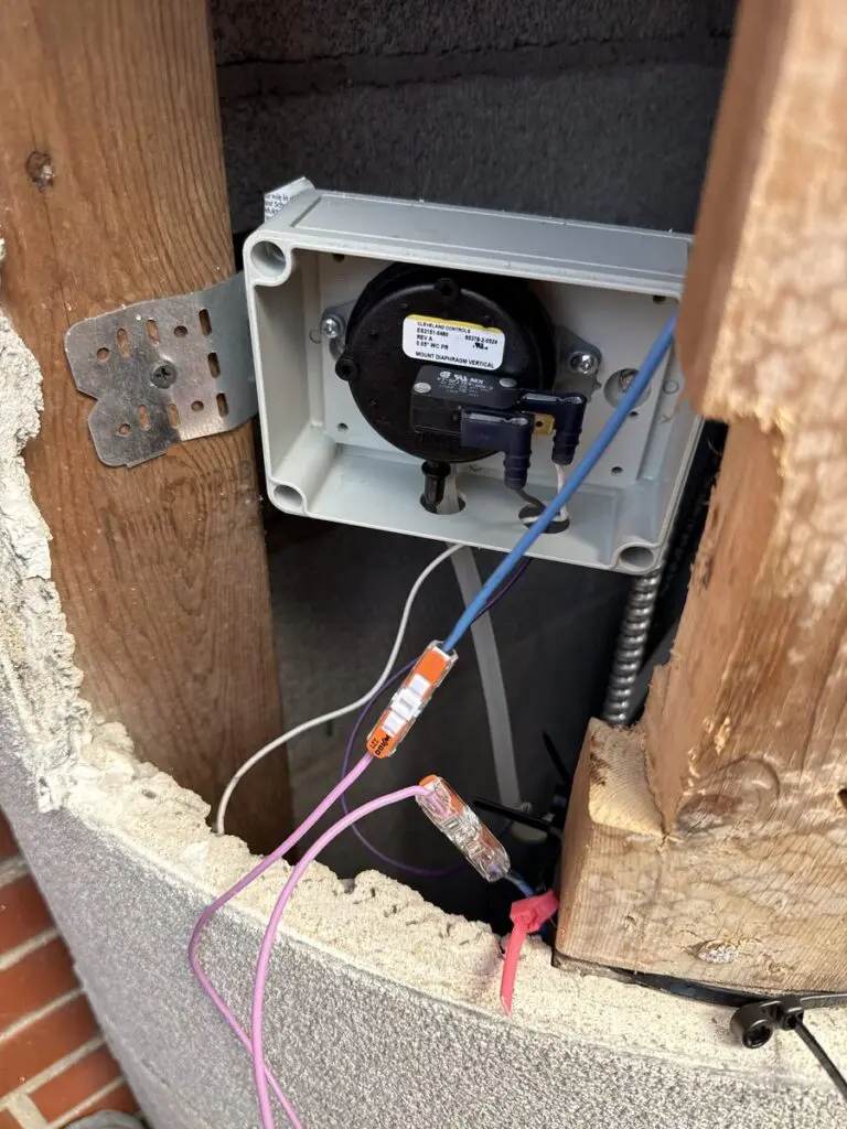 Vent pressure switch mounted in the wall framing during a gas fireplace installation, with wiring connections