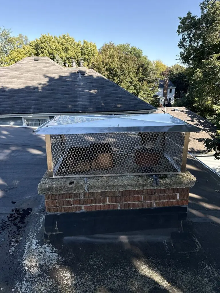Stainless steel multi-flue chimney cap with mesh screen over clay flue tiles on a brick chimney on a flat roof