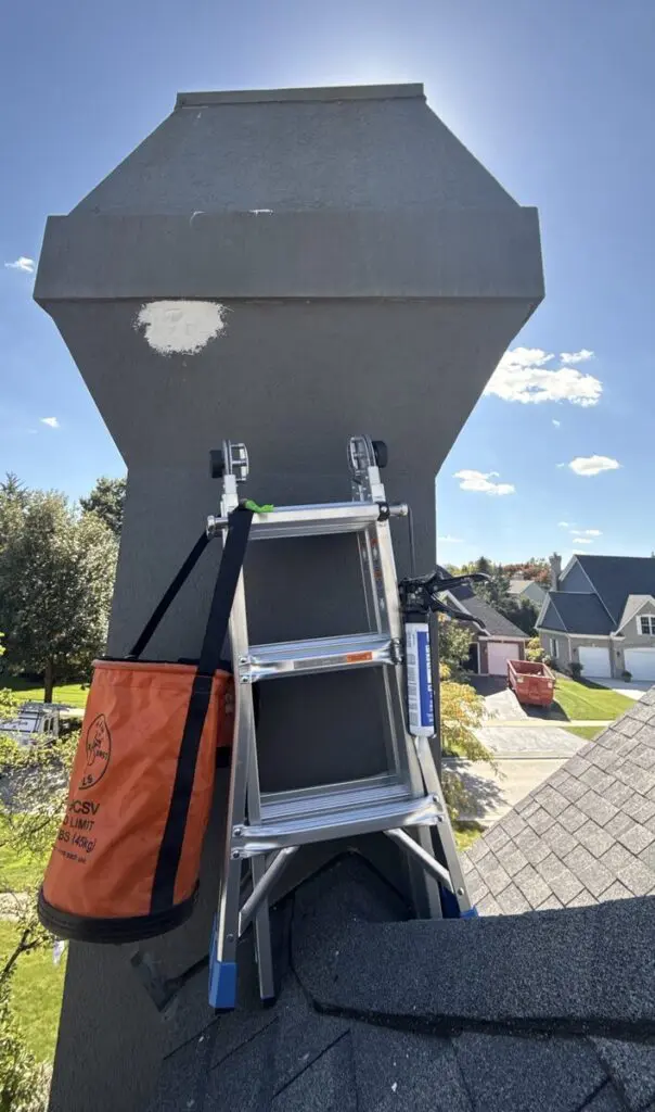 Stucco chimney chase with a fresh patch repair, ladder set up on the roof for access